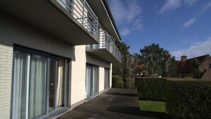 Een modern gebouw met grote ramen, een houten terras en een verzorgde haag.