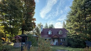 Ett hus med ett rött tegeltak, omgivet av täta träd och en gräsklädd trädgård.