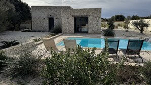 Et stenhus med swimmingpool og udendørs siddepladser.