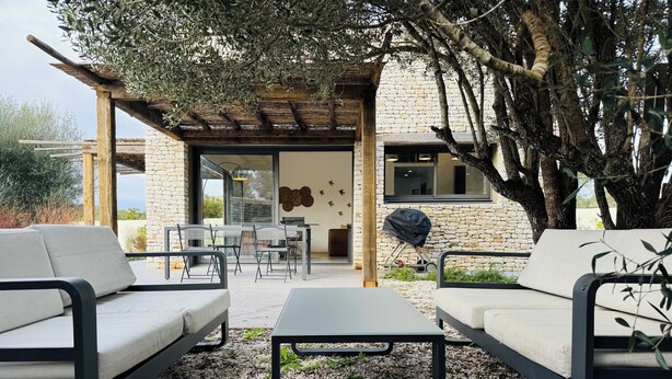 Et udendørs opholdsområde med to sofaer og et bord, en pergola samt en bygning i sten i baggrunden.