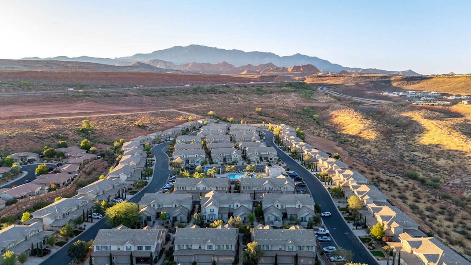 A residential area with houses arranged in a grid pattern, a winding road, and mountains in the background.