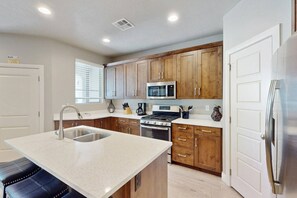 A modern kitchen with wooden cabinets, stainless steel appliances, a central island with a sink, and a black bar stool. - 3BR/2.5BA Townhouse w/ Pool & Hot Tub (Washington)