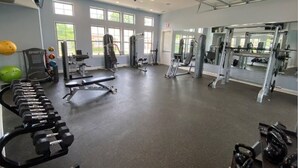 Uma academia ampla com diversos equipamentos de exercício, grandes janelas e pé direito alto.