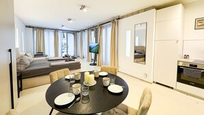 Una sala de estar moderna con un sofá, una mesa de comedor para cuatro personas y una cocina con refrigerador y horno.