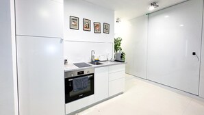 Una cocina moderna con armarios blancos, un horno Bosch, un lavamanos y una cafetera. Hay cuadros en la pared y una planta en la encimera.