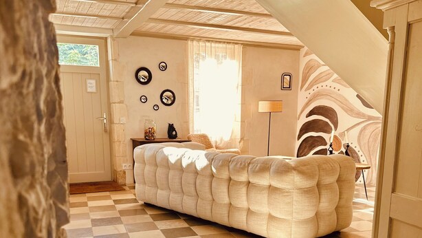 Una habitación acogedora con un sofá grande y capitonado, suelo a cuadros y una ventana con cortinas.