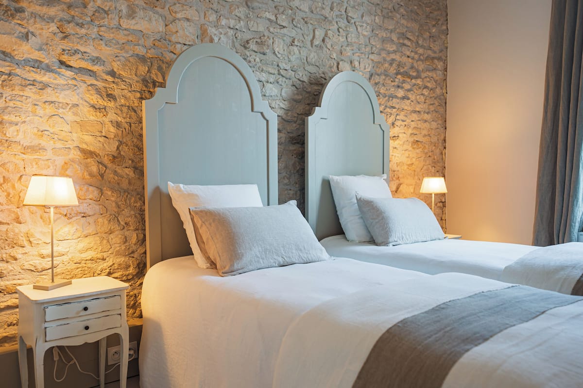 Un dormitorio con dos camas, pared de piedra y lámparas de noche.