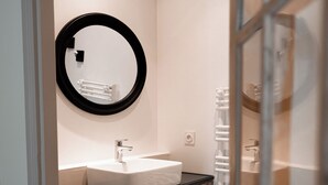 Un baño con un lavamanos blanco, un espejo con marco negro y un perchero para toallas.