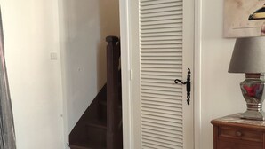 Ein Zimmer mit einem gemusterten Boden, einem roten Sessel, einem Glastisch, einem Holznachttisch und einer weißen Tür mit schwarzem Griff.