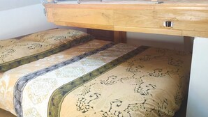 Ein Schlafzimmer mit einem hölzernen Bettgestell, zwei Betten mit gemusterten Bettbezügen und einer hölzernen Kommode mit einer Schublade.