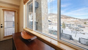 Una habitación con un ventanal grande, un banco de madera y vistas a un estacionamiento y montañas.