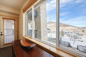 A room with a large window, a wooden bench, and a view of a parking lot and mountains. - Heart of Canyons Village Walk to Lifts 226 (Park City)