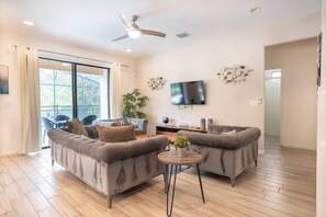 A modern living room with two sofas, a coffee table, a TV, and a large window. - Veranda Palms 6BR  Pool  Near Disney Parks (Kissimmee)