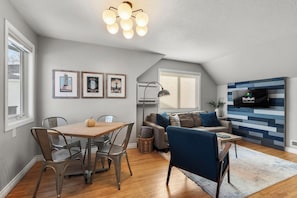 Een moderne woonkamer met een eettafel, stoelen, een bank, een televisie en ingelijste foto's aan de muur.