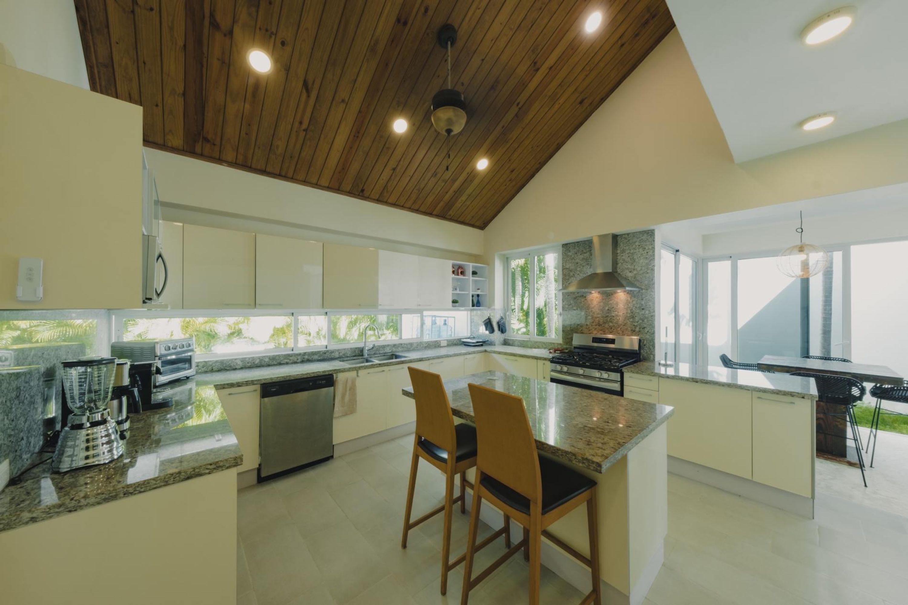 Une cuisine moderne avec un plafond en bois, des plans de travail en granit et un îlot central doté de deux chaises.