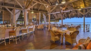 Un área de comedor al aire libre con mesas de madera y sillas de mimbre, con vista a una playa.