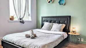 Een moderne slaapkamer met een zwart bekleden bed, een nachtkastje met een lamp en geometrische wanddecoratie.