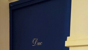 Een blauwe gesloten deur met een deurklink en een klein plaquette waarop 'Duc' staat.