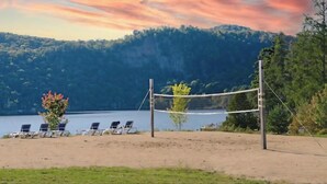 Cancha de voleibol de playa con sillas y una red, rodeada de árboles y un lago.