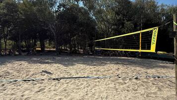 Una playa arenosa con una red de voleibol y árboles al fondo.