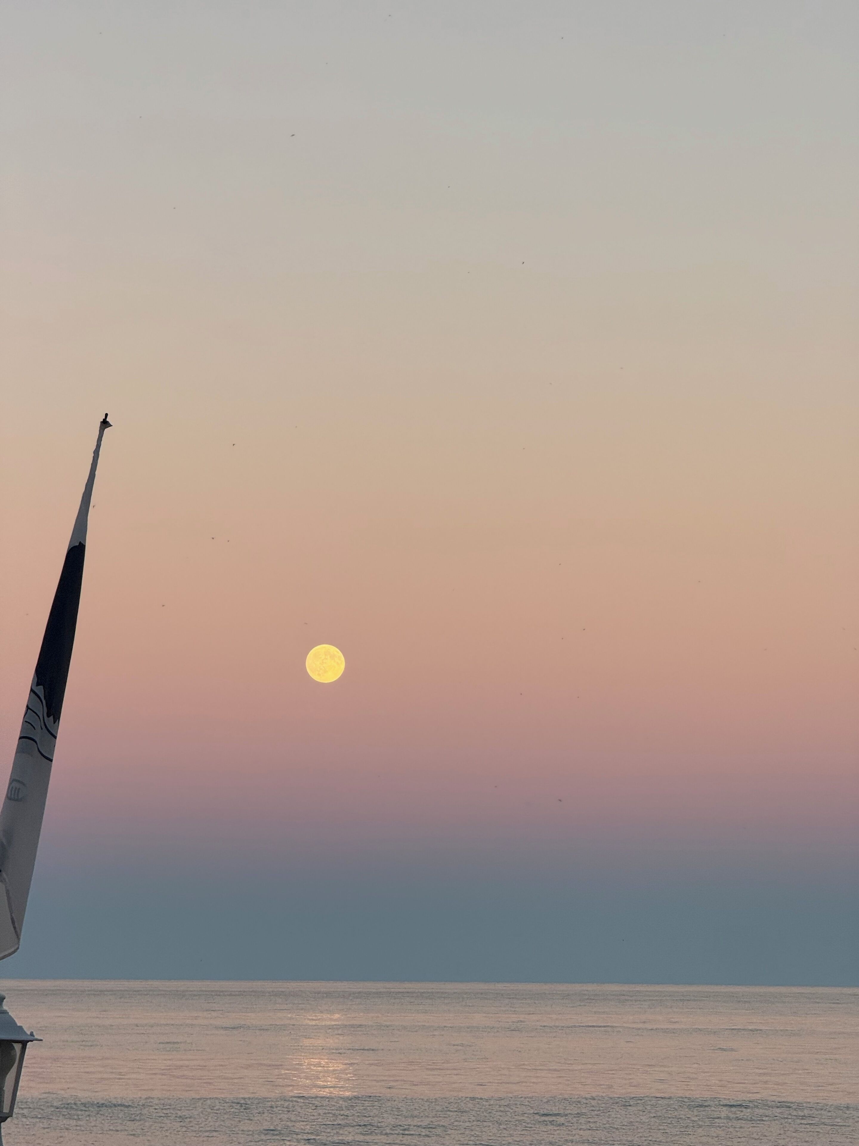 A sunset over a calm sea with a sailboat's mast and a small boat in the foreground.