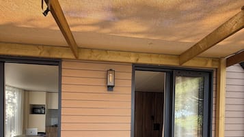 Una terraza de madera con un ventanal corredero que da a un dormitorio con cama y ventana.