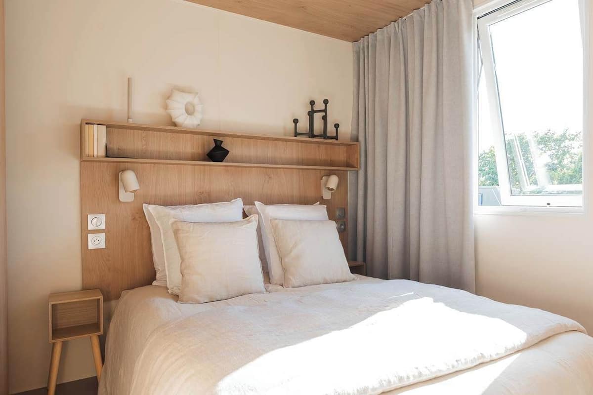 A neatly made bed with a headboard, a bedside table, and a window with curtains.