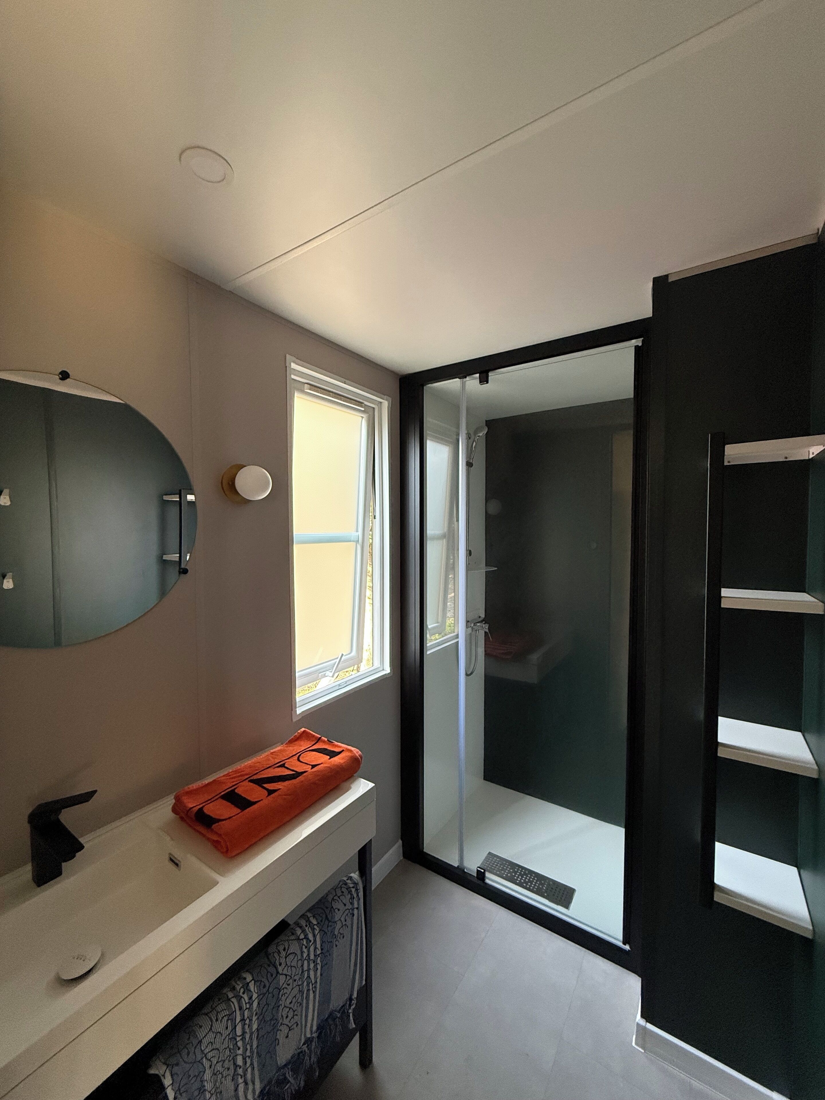 Un baño moderno con un espejo grande, un lavamanos blanco y una zona de ducha con puerta de vidrio.