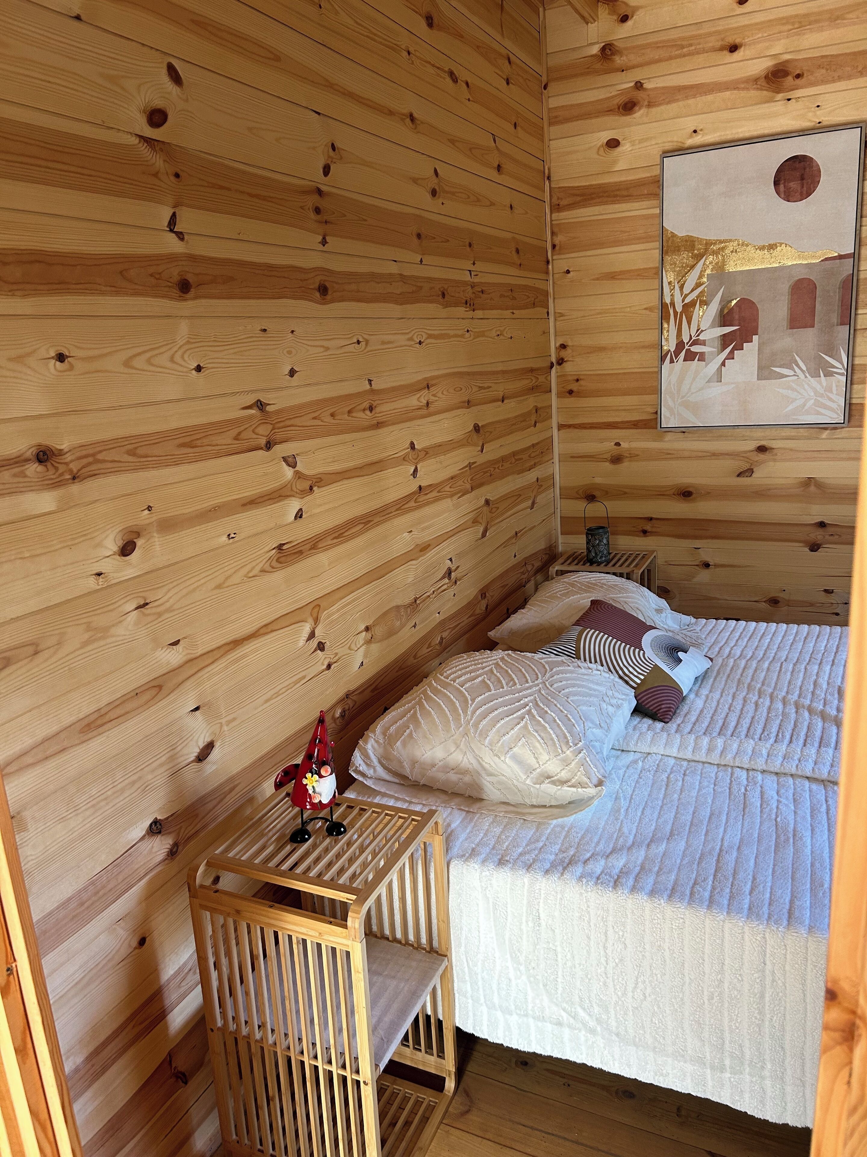 Une pièce de cabane en bois comprenant un lit, des oreillers, une petite table et un berceau.