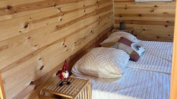 A wooden cabin room with a bed, pillows, a small table, and a crib.