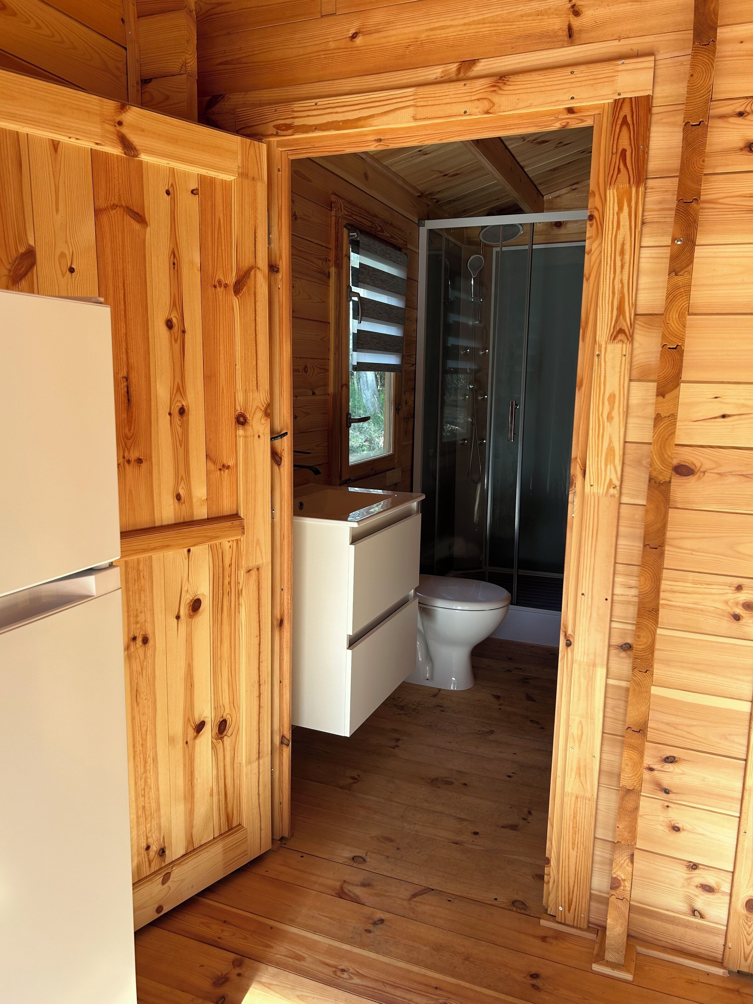 L’intérieur d’une cabane en bois comprend un coin cuisine, un réfrigérateur blanc, un évier et des toilettes.