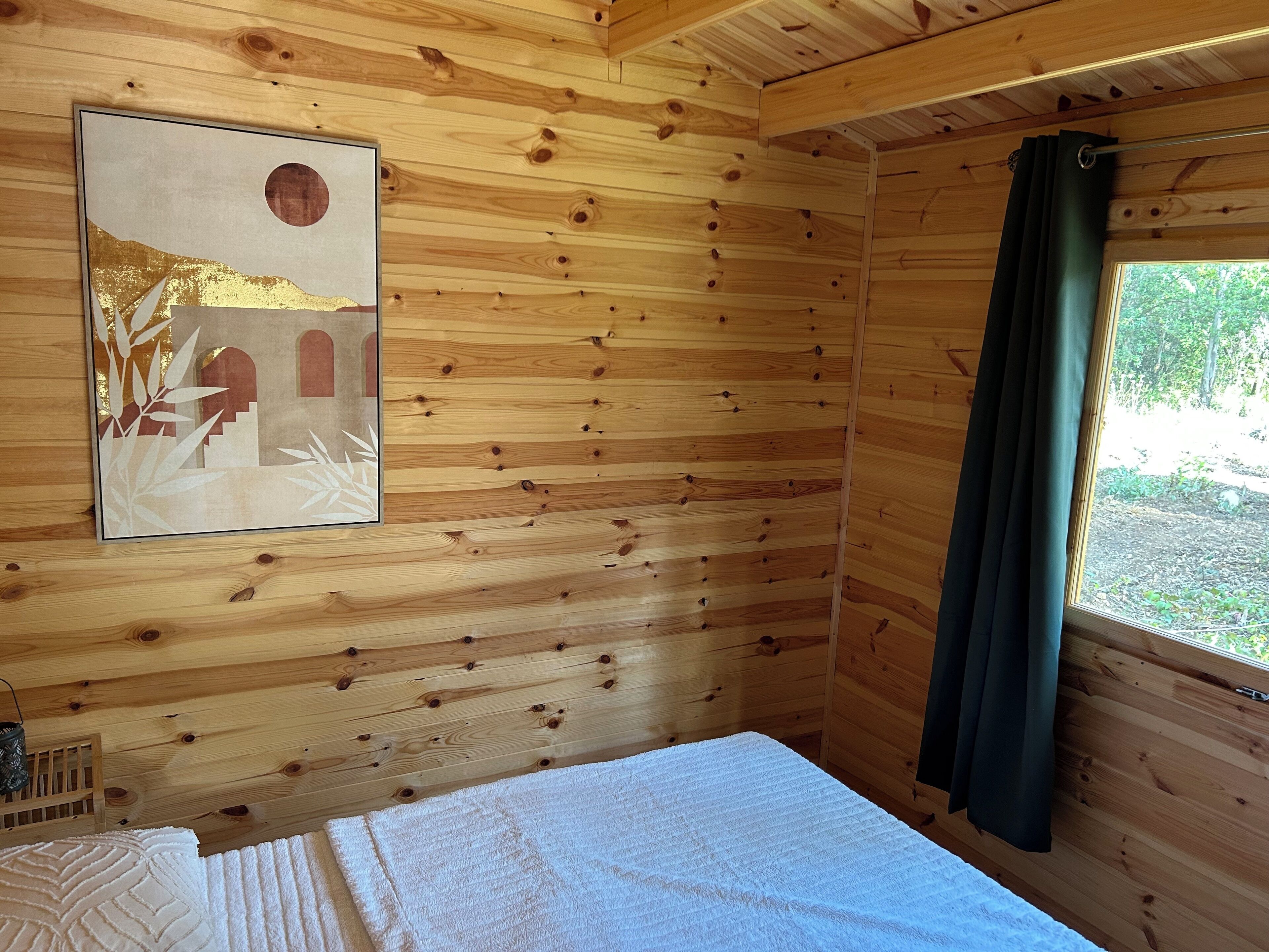 Een houten kamer met een bed, een ingelijste foto aan de muur en een raam met gordijn.