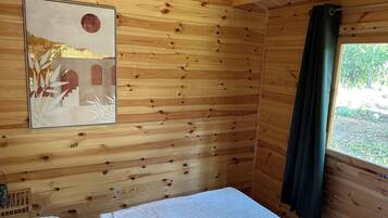 Een houten kamer met een bed, een ingelijste foto aan de muur en een raam met gordijn.