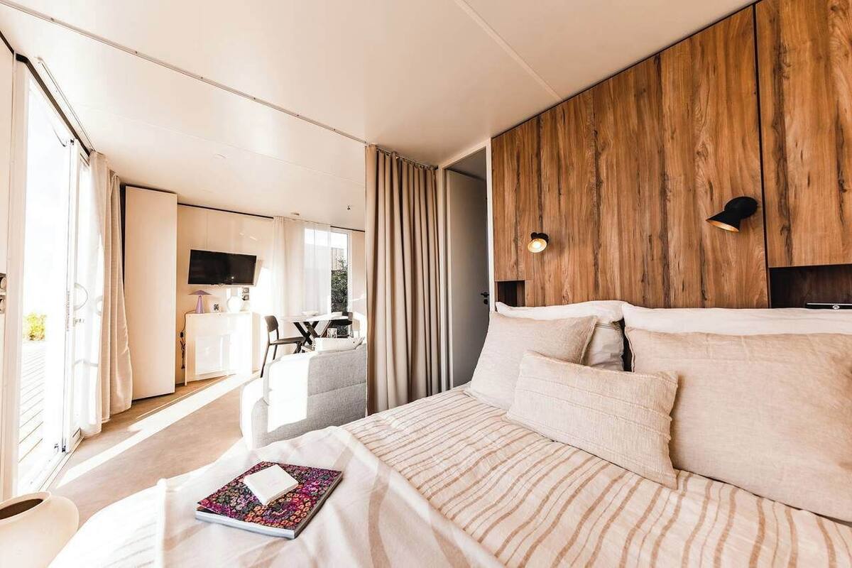 A modern hotel room with a large bed, a wooden accent wall, a desk with a chair, and a television.