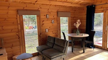 A wooden cabin interior with a sofa, a small table, and a dining table with chairs.