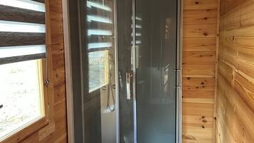 Un baño de cabaña de madera con ducha envuelta en vidrio, un inodoro y una ventana con persianas.