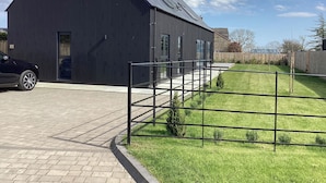 A modern building with a dark exterior, a paved driveway, and a grassy area with a metal fence. - The Barn (Morpeth)