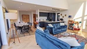 A spacious living area with a blue sofa, a dining table set for six, and a kitchen in the background. - The Barn (Morpeth)