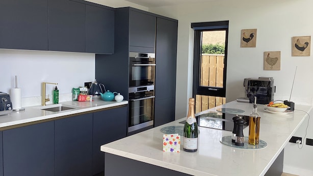 A modern kitchen with dark cabinets, a central island, a coffee machine, and a view of the outdoors. - The Barn (Morpeth)