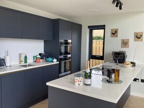 Una cocina moderna con armarios oscuros, una isla central, una cafetera y vistas al exterior.
