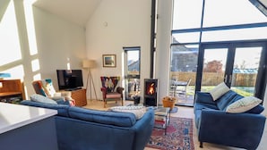 A spacious living room with a large TV, comfortable seating, a fireplace, and a view of the outdoors. - The Barn (Morpeth)