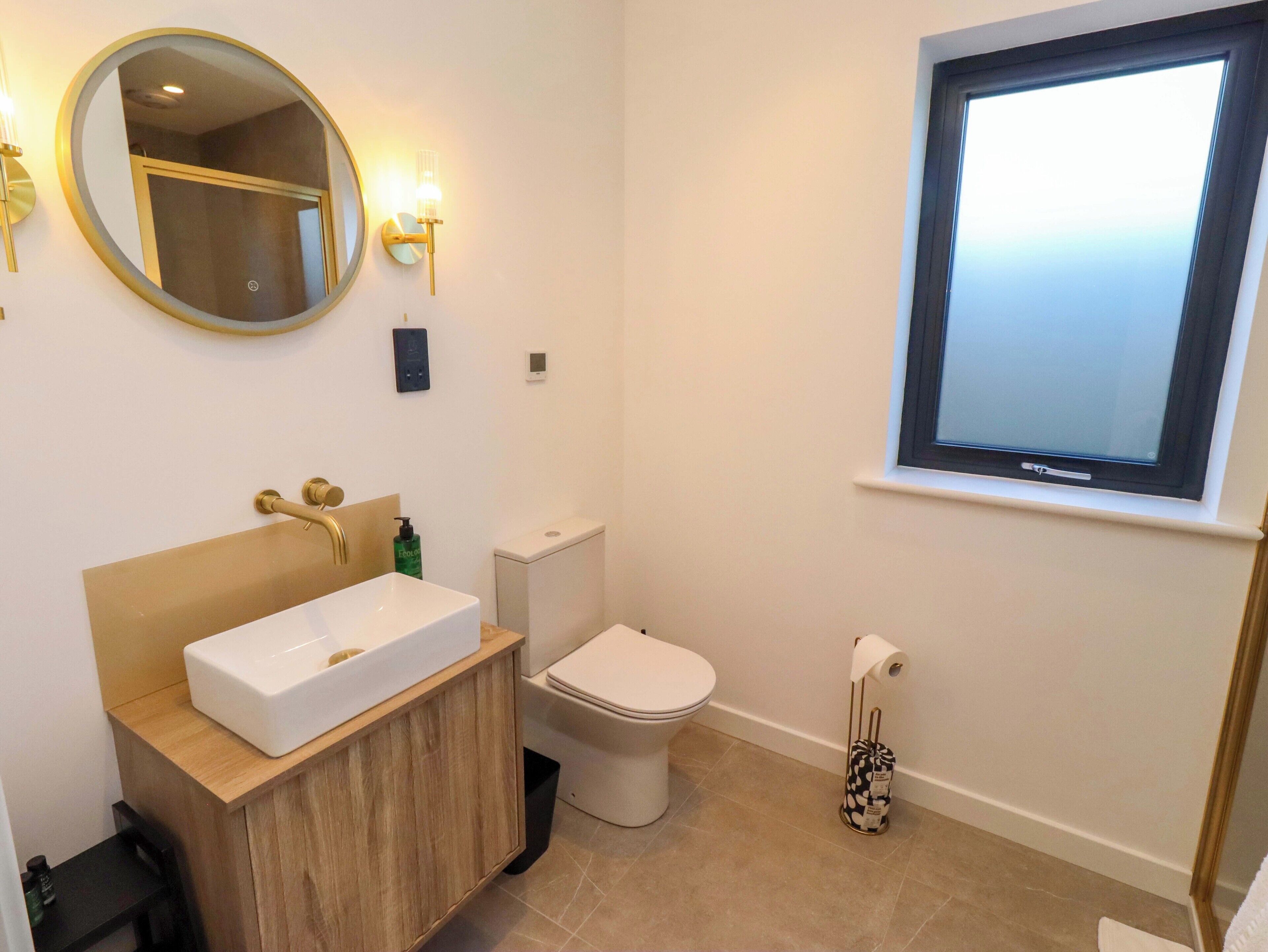 A bathroom with a white sink, wooden vanity, a toilet, and a window with a view.