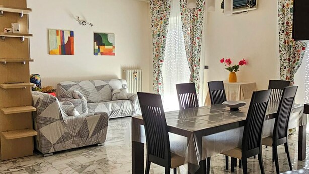 Ein Wohnzimmer mit einer Couch, einem Esstisch mit Stühlen und einem Fernseher an der Wand.