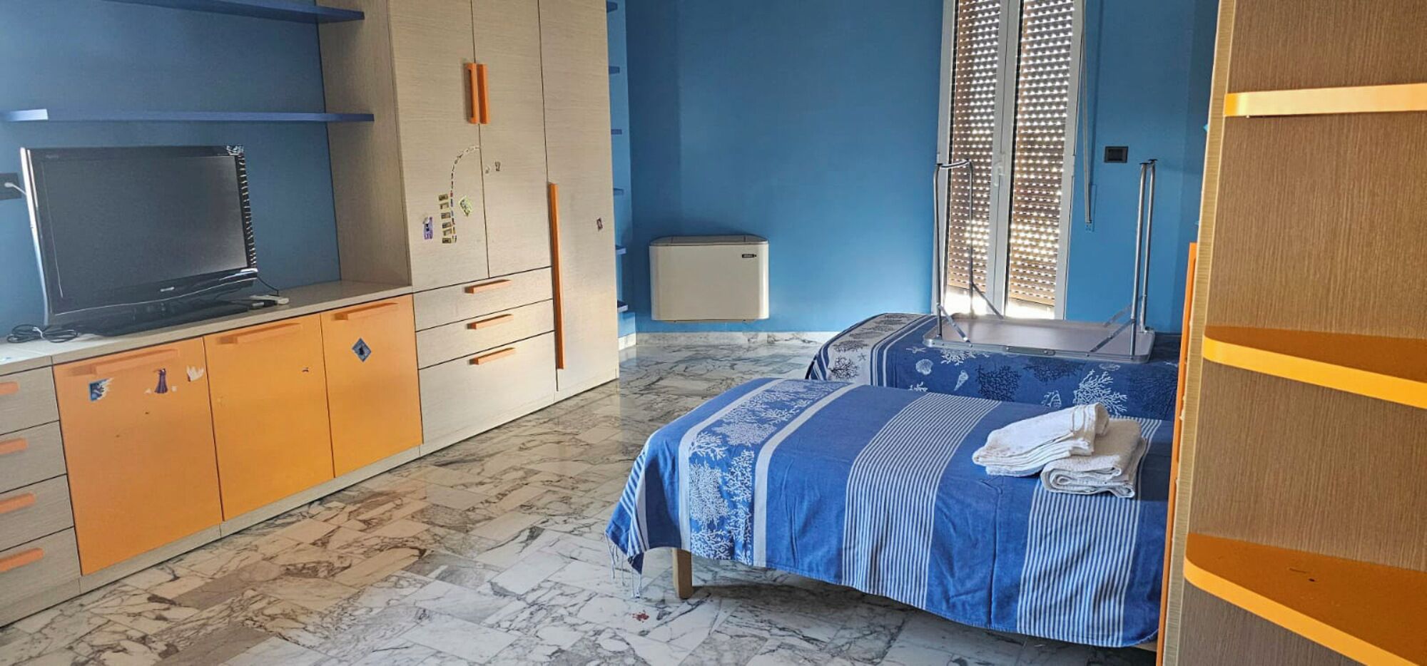 A bedroom with a bed, a wardrobe, a television, and a small heater.