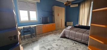 Un dormitorio con cama, escritorio con silla, armario y ventana con cortinas.