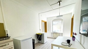 Een compacte keuken met een koelkast, een klein spoelgedeelte, een eettafel met stoelen en een raam dat zorgt voor daglicht.