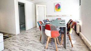 Een eethoek met een tafel gedekt voor zes personen, omringd door kleurrijke stoelen, een plafondventilator en een schilderij aan de muur.