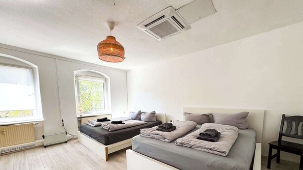 Een slaapkamer met twee bedden, een radiator, een raam en een hanglamp.