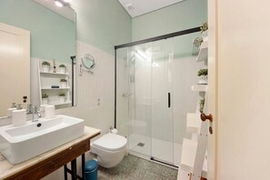 Et badeværelse med en hvid vask, toilet og glasafskærmet brusekabine.