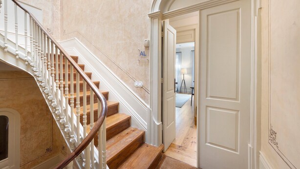Una escalera con barandilla blanca y peldaños de madera que conduce a una habitación con una puerta marcada 'AL'.